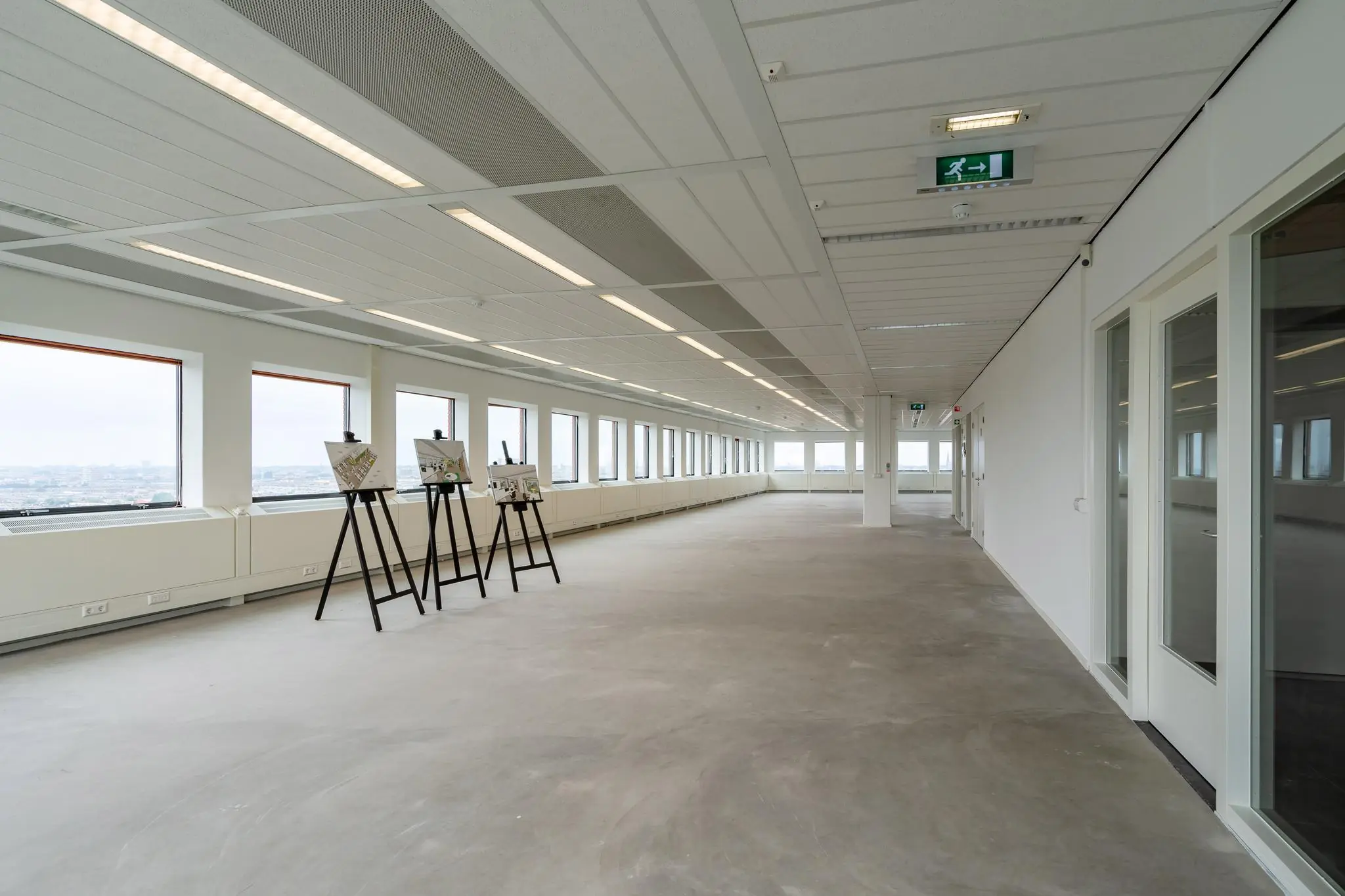 Lichte, lege kantoorruimte aan het Johanna Westerdijkplein met grote ramen en enkele schildersezels met presentaties.